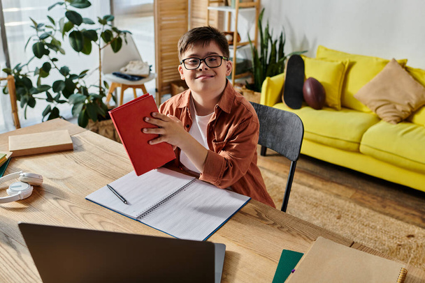 Ein Junge mit Down-Syndrom sitzt an einem Schreibtisch und konzentriert sich auf sein Notizbuch und seinen Laptop. - Foto, Bild