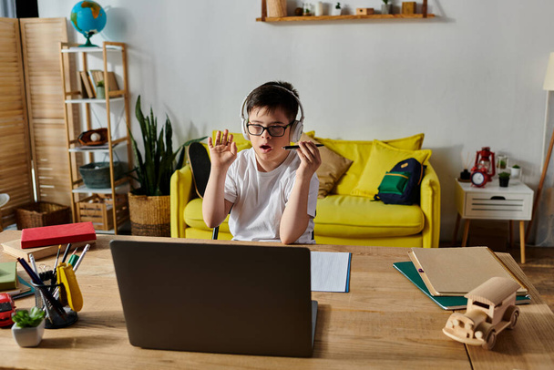 Мальчик с синдромом Дауна сидит за столом, сосредоточенный на использовании ноутбука. - Фото, изображение