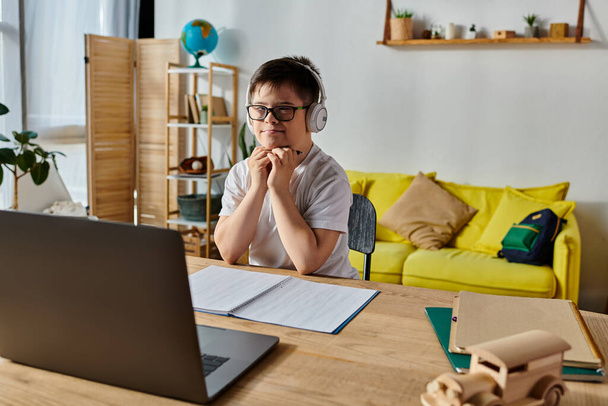 schattige jongen met Down syndroom dragen van een koptelefoon, verdiept in het gebruik van laptop aan het bureau. - Foto, afbeelding