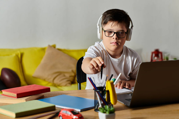 очаровательный мальчик с синдромом Дауна сидит за столом, взаимодействуя с ноутбуком. - Фото, изображение