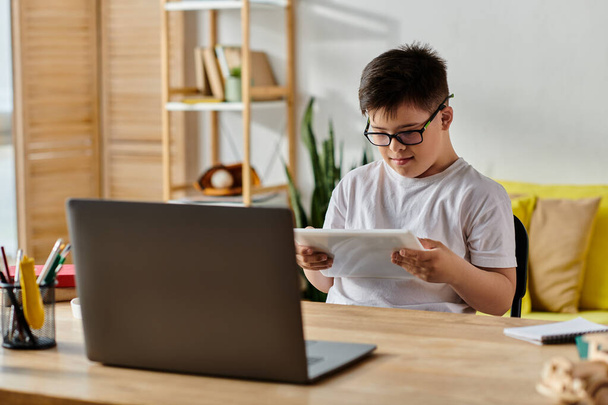 entzückender Junge mit Down-Syndrom mit Brille in Laptop-Aktivitäten zu Hause eingetaucht. - Foto, Bild