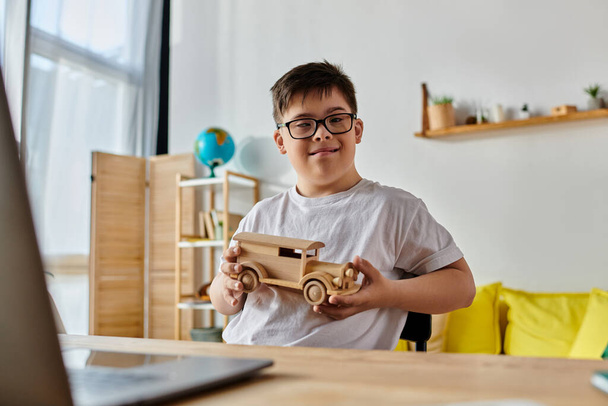 Down sendromlu sevimli çocuk dizüstü bilgisayarın önünde tahta bir oyuncak arabayla oynuyor.. - Fotoğraf, Görsel