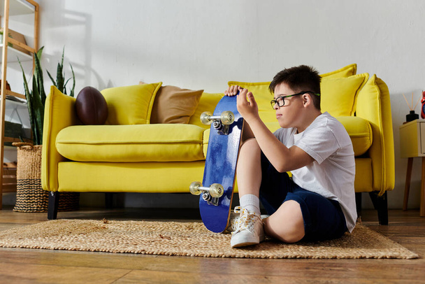 adorable garçon avec trisomie 21 heureusement assis sur le sol avec une planche à roulettes dans sa chambre. - Photo, image