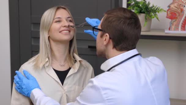 Un giovane otorinolaringoiatra attraente che esamina il naso di un giovane paziente durante una visita medica nello studio ENT - Filmati, video