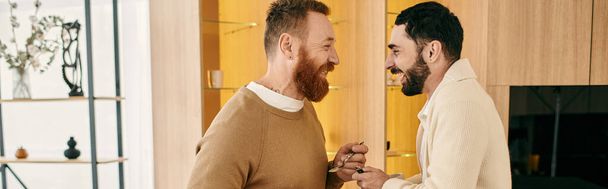 Δύο άνδρες όρθιοι, μοιράζονται μια στιγμή σύνδεσης και αγάπης σε ένα μοντέρνο διαμέρισμα. - Φωτογραφία, εικόνα