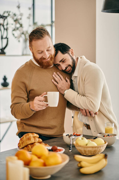 Dos hombres comparten un cálido abrazo en la cocina de un apartamento moderno, expresando su amor y felicidad en los brazos del otro. - Foto, imagen