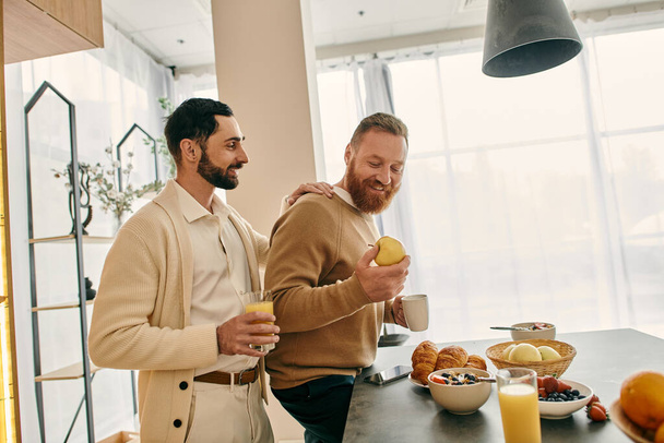 Um casal gay feliz se senta em uma mesa em uma cozinha moderna, compartilhando café da manhã e conversa em um momento de amor e união. - Foto, Imagem