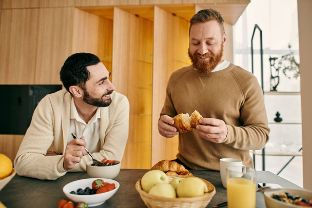 Two men, a happy gay couple, sit at a kitchen table enjoying breakfast in their modern apartment. - Foto, Bild