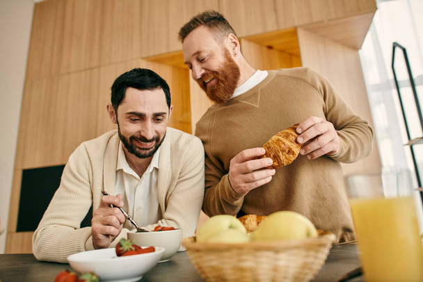 Dva šťastní muži, homosexuální pár, sedí u útulného kuchyňského stolu, vychutnávají si snídani a každý druhý společnost v moderním bytě. - Fotografie, Obrázek