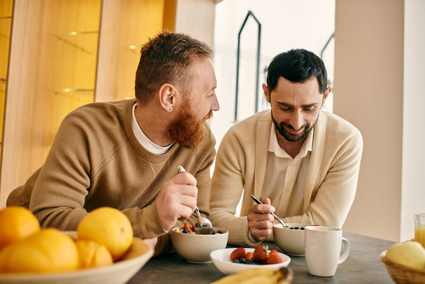 Deux hommes, un couple gay heureux, profitent d'un petit déjeuner confortable ensemble dans leur appartement moderne. - Photo, image