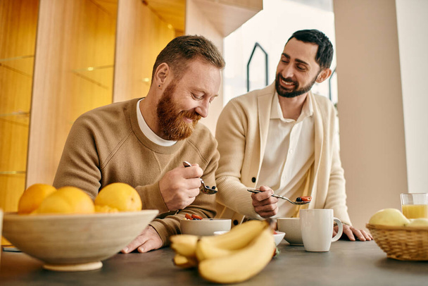 Deux hommes barbus, un couple gay heureux, partageant un repas dans une cuisine moderne. - Photo, image