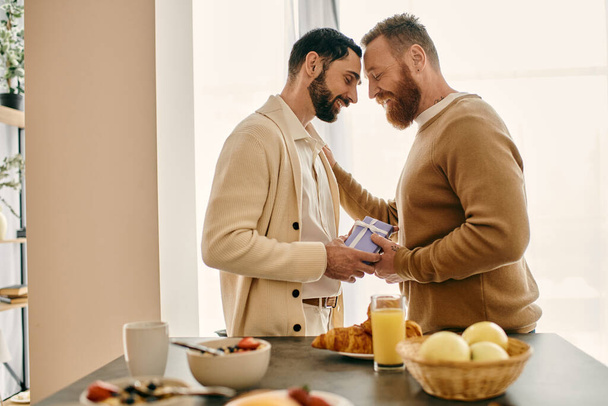 Δύο γενειοφόροι άνδρες στέκονται σε μια κουζίνα, μοιράζονται μια στιγμή ευδαιμονίας και σύνδεσης στο μοντέρνο διαμέρισμά τους. - Φωτογραφία, εικόνα