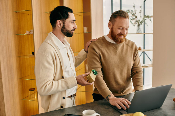 Dos hombres, una feliz pareja gay, absortos en su portátil en una cocina moderna, disfrutando de tiempo de calidad juntos. - Foto, Imagen
