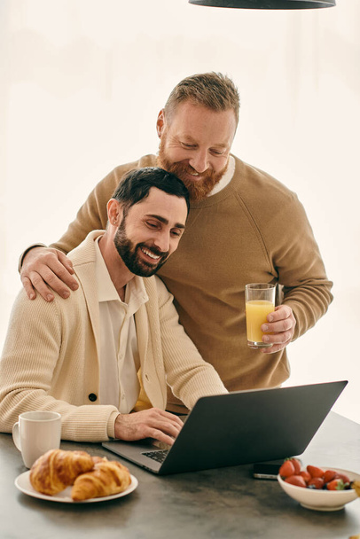 İki adam, mutlu bir eşcinsel çift, bir dizüstü bilgisayarla bir masada oturuyorlar, işleriyle meşguller. Onlar da bir bardak portakal suyu içiyorlar.. - Fotoğraf, Görsel