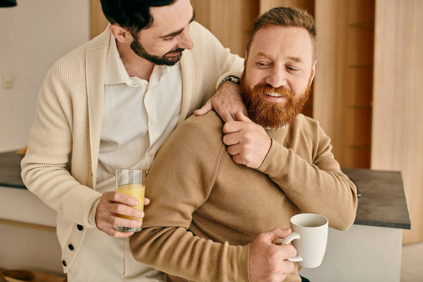 Due uomini, parte di una coppia gay felice, si abbracciano calorosamente in una cucina moderna, condividendo un momento di amore e connessione. - Foto, immagini