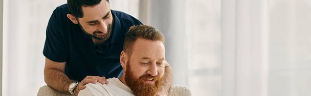 Casual gay couple in modern living room, one man with a beard sits on a couch next to his partner. - Foto, Bild