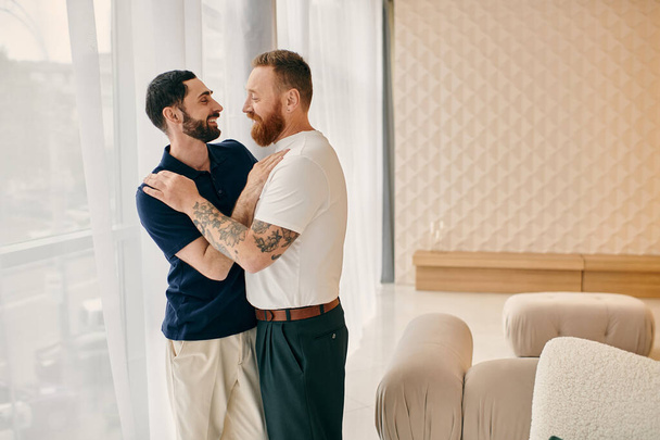 A happy gay couple embraces in a modern living room, dressed in casual clothes, enjoying quality time together. - Photo, Image