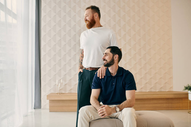 Dva muži v neformálním oblečení sedí na gauči v moderním obývacím pokoji a užívají si spolu kvalitní čas. - Fotografie, Obrázek