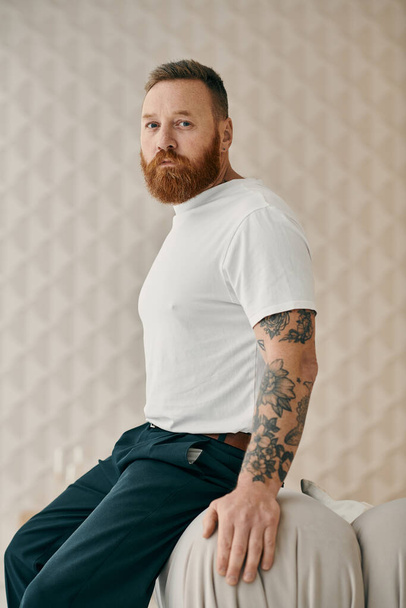 Un homme avec une barbe s'assoit confortablement, perdu dans la pensée, dans un cadre de salon moderne. - Photo, image
