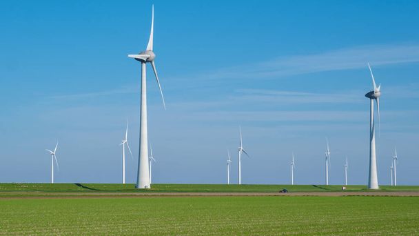 A serene field of vibrant green grass stretches out before us, dotted with a collection of majestic windmills spinning gracefully in the background. - Photo, Image