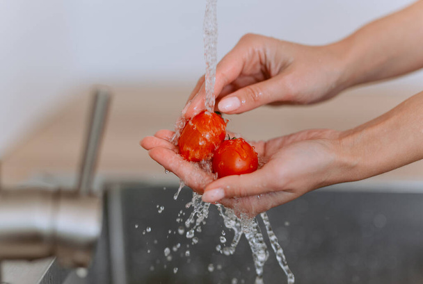 Закрыть свежие овощи. Женские руки моют помидоры черри с водой на кухне. - Фото, изображение