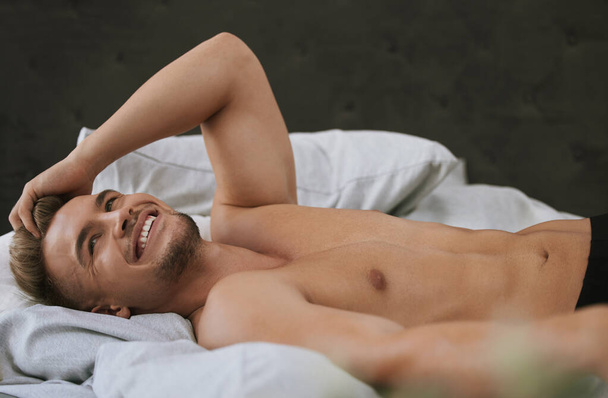 Morning, wake up or happy man in bedroom thinking of resting in home, house or apartment. Topless, relax or calm male person sleeping on break with smile or ready to start day or chill on weekend. - Photo, Image