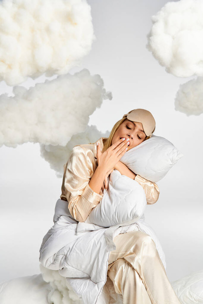 A dreamy blonde woman in cozy pajamas sits peacefully atop fluffy clouds. - Zdjęcie, obraz