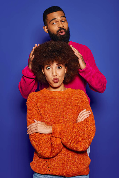 Jonge Afro-Amerikaanse man en vrouw in levendige kleding staan samen tegen een blauwe achtergrond, presenteren hun vriendschap. - Foto, afbeelding