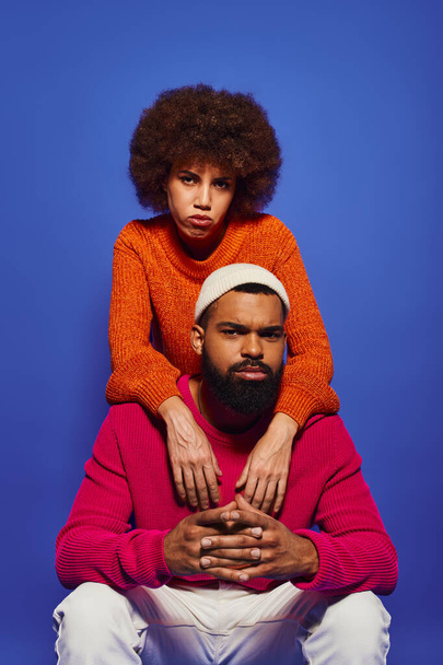 Young African American friends in casual attire, woman sitting atop mans shoulders against a blue background. - Photo, Image