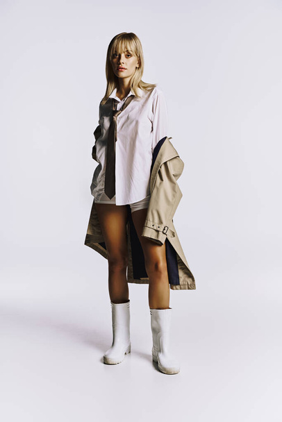 Stylish woman combines short shorts and trench coat in striking pose. - Photo, Image