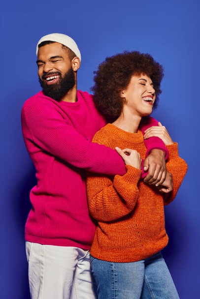 Jovens amigos afro-americanos abraçam calorosamente em trajes vibrantes, mostrando um belo vínculo de amizade em um fundo azul. - Foto, Imagem
