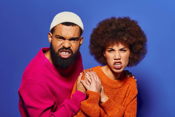 Un giovane afroamericano uomo e donna, amici in abiti casual vibrante, colpisce una posa insieme su uno sfondo blu. - Foto, immagini