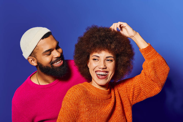 Egy fiatal afro-amerikai férfi és nő, mindkettő afro hajjal, élénk ruhába öltözve, örömöt és barátságot árasztva kék alapon.. - Fotó, kép