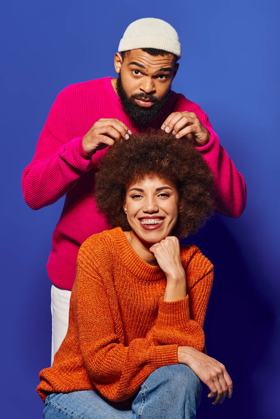 Un jeune homme et une jeune femme afro-américaine assis ensemble, mettant en valeur des vêtements décontractés dynamiques et un lien d'amitié fort sur un fond bleu. - Photo, image