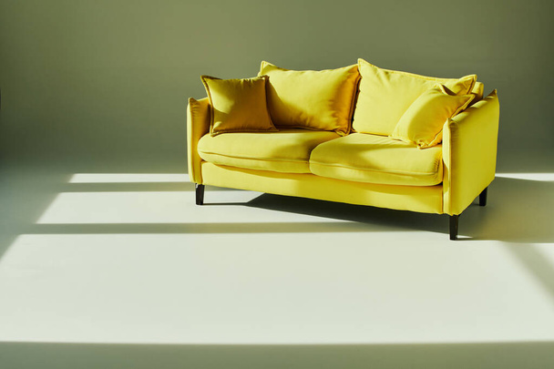 Яскравий жовтий диван контрастує з чистою білою підлогою, створюючи яскравий і привабливий простір. - Фото, зображення