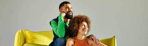 Друзья-афроамериканцы в разноцветной одежде делят момент дружбы на жёлтом диване на сером фоне. - Фото, изображение