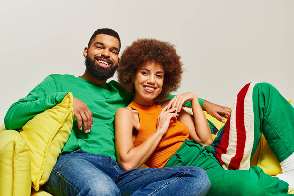 Szczęśliwi Afroamerykanie przyjaciele w żywe ubrania siedzi na krześle worek żółtej fasoli, emanuje ciepło i bliskość. - Zdjęcie, obraz