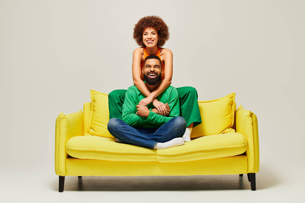 Szczęśliwi Afroamerykanie w żywych ciuchach siedzący na żółtej kanapie, ucieleśniający istotę przyjaźni mężczyzny i kobiety. - Zdjęcie, obraz