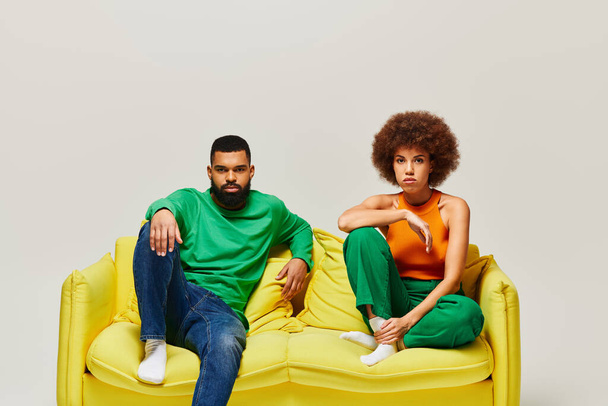 Amici afroamericani in abiti vibranti siedono su un divano giallo, mostrando amicizia tra un uomo e una donna. - Foto, immagini
