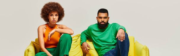 Афроамериканские друзья в яркой одежде сидят на жёлтом диване, демонстрируют крепкую дружескую связь. - Фото, изображение