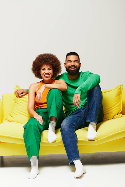 Felices amigos afroamericanos con ropa vibrante se sientan en un sofá amarillo, mostrando una conexión cálida. - Foto, Imagen