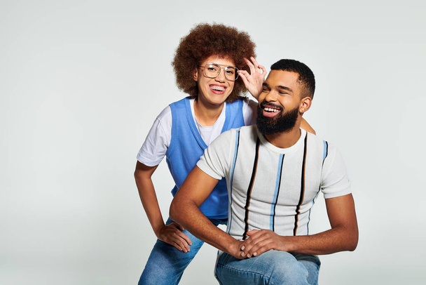 Stijlvolle Afro-Amerikaanse man en vrouw omarmen vriendschap in een modieuze pose tegen een grijze achtergrond. - Foto, afbeelding
