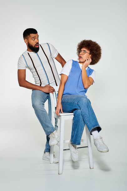 Ένας Αφρο-Αμερικανός άντρας και μια γυναίκα με στυλάτη ενδυμασία, κάθονται στα σκαμπό δίπλα-δίπλα, επιδεικνύοντας φιλία και συντροφικότητα. - Φωτογραφία, εικόνα