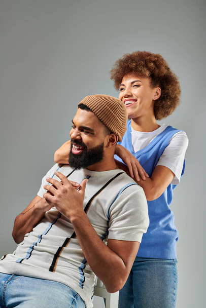 A stylish African American man sitting on top of a chair next to a woman against a grey background, showcasing a unique friendship. - Photo, Image