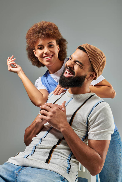 Стильно одягнений афроамериканський чоловік сидить на стільці з жінкою на спині, демонструючи унікальний момент дружби. - Фото, зображення