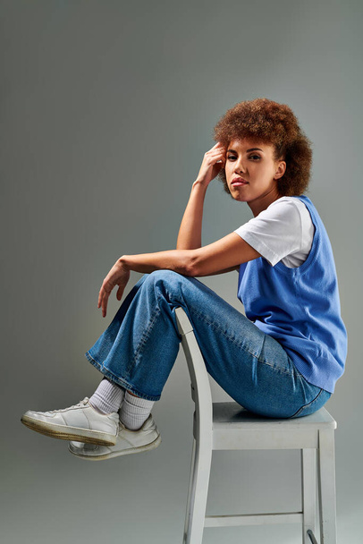 Una donna di colore elegantemente seduta su una sedia bianca incontaminata, trasudante grazia e portamento su uno sfondo neutro. - Foto, immagini