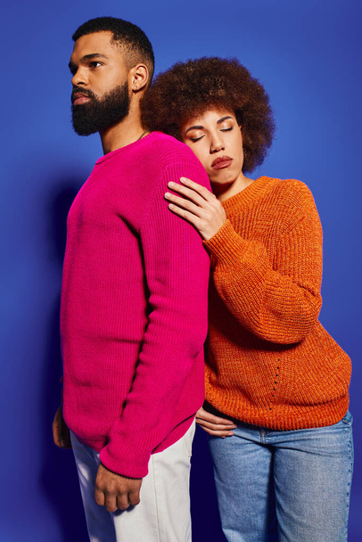 Egy fiatal afro-amerikai férfi és nő, barátok élénk alkalmi öltözékben, együtt állnak kék háttérben.. - Fotó, kép