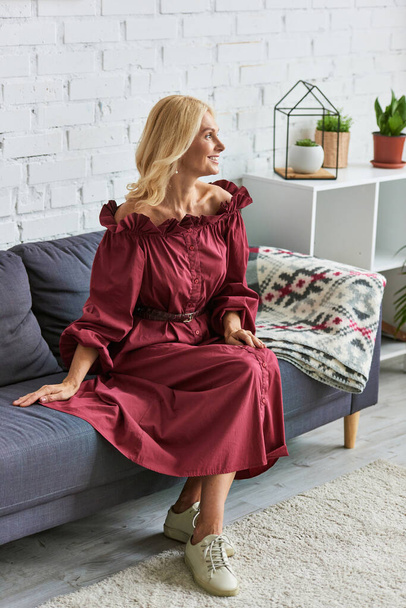 Mujer con estilo en vestido rojo sentado en el sofá. - Foto, Imagen