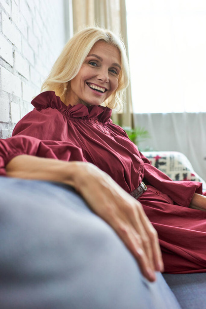 Stilvolle Frau in schicker Kleidung lächelt, während sie auf der Couch sitzt. - Foto, Bild