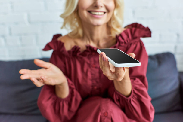 Mujer madura en traje elegante sentada en el sofá, absorta en el teléfono celular. - Foto, imagen